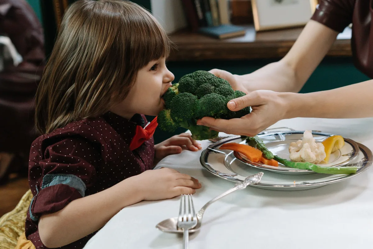 Enfant mangeant des légumes à table lors d'un repas en famille.