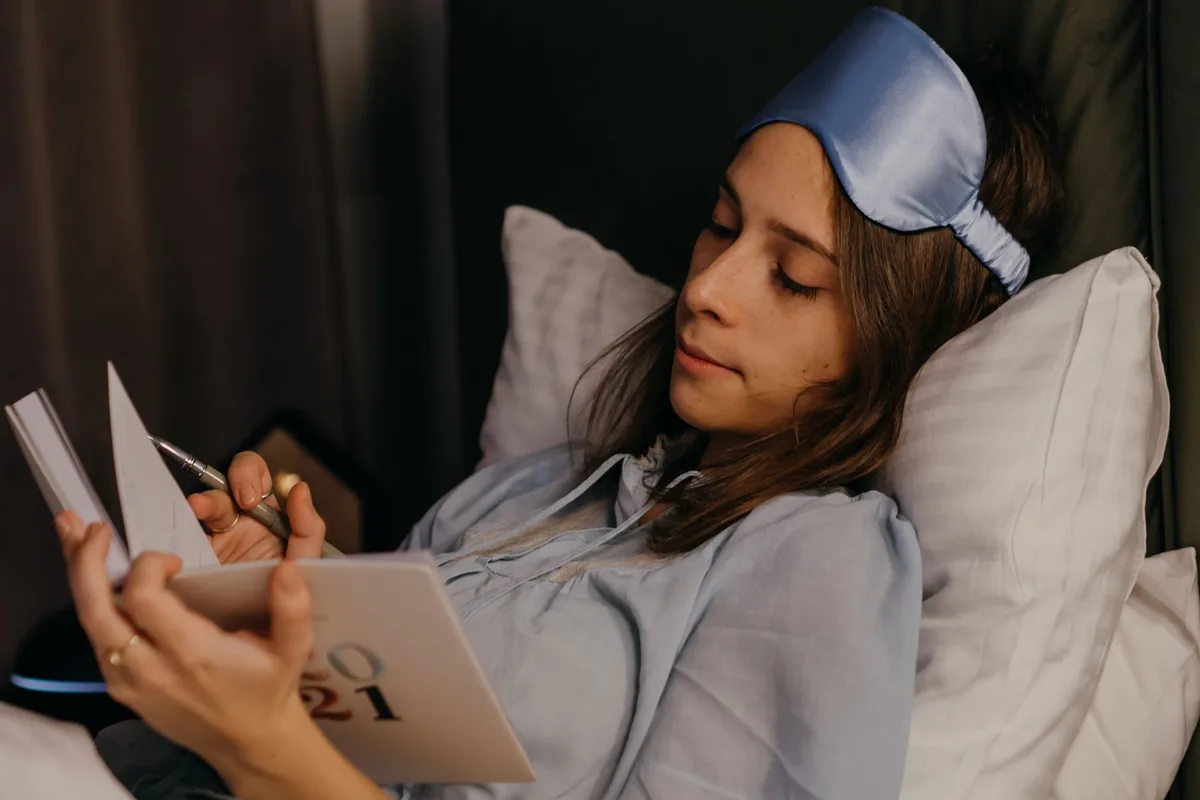 Carnet de suivi du sommeil ouvert sur une table de nuit avec stylo et réveil