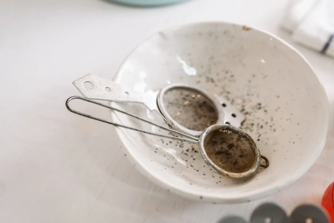 Grains de quinoa rincés sous l'eau dans une passoire fine, avec des gouttelettes d'eau claire.