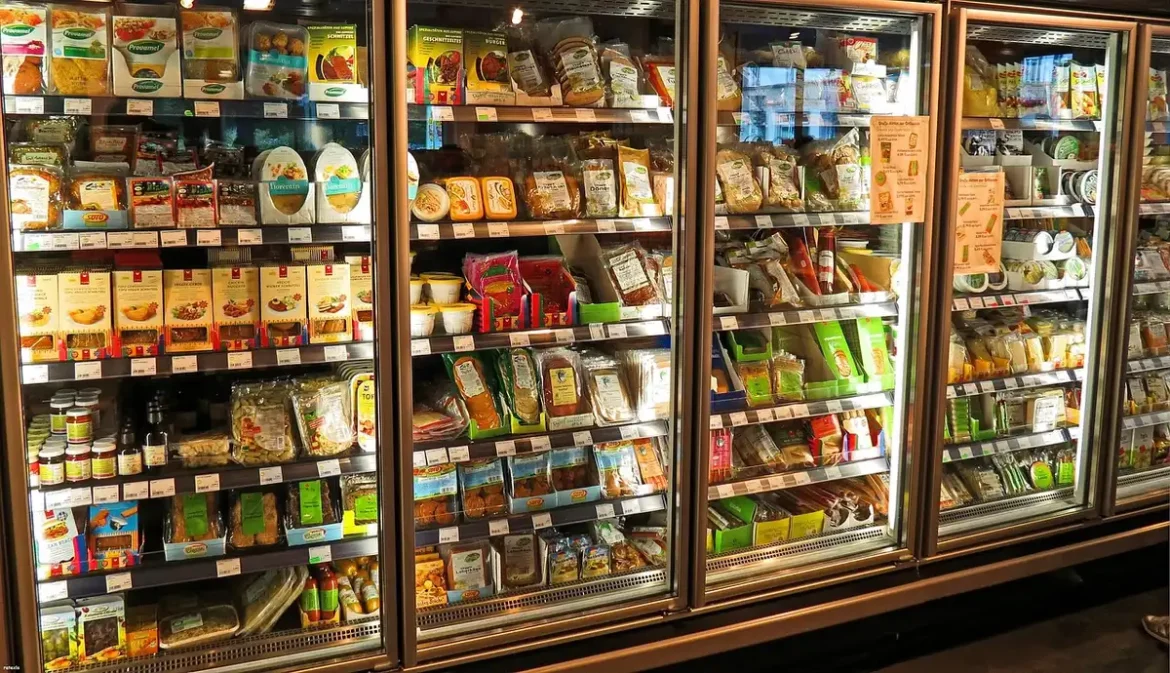 Main prenant un bac de carottes râpées dans une allée de supermarché en plein jour
